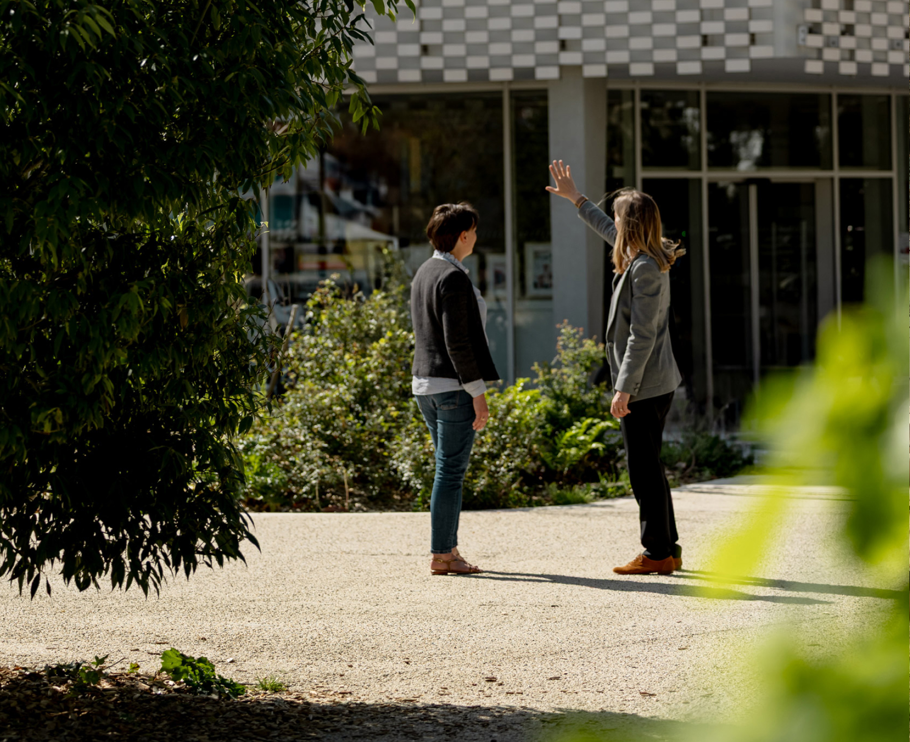 Photo de Léna avec une cliente positionnées devant un bâtiment moderne et arboré.